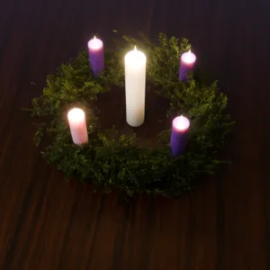 Advent wreath with lit candles in purple and white viewed from above on wooden surface